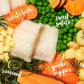 Raw white fish fillets with sweet potatoes, carrots, green peas, and seaweed on a bed of garden veggies.