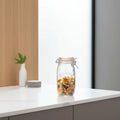 A Kilner glass clamp-lid jar filled with rotini pasta, styled on a marble surface with kitchen ingredients and bottles in the background.