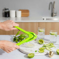 Person using a green citrus squeezer on a white plate with sliced limes and cucumbers.