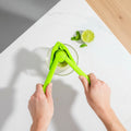 Person using a green citrus press on a white plate with sliced limes and cucumbers.