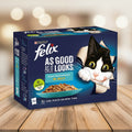 A box of Purina Felix cat food, Ocean Feast Selection in Jelly, featuring a black and white cat peeking out of the packaging on a dark blue background.