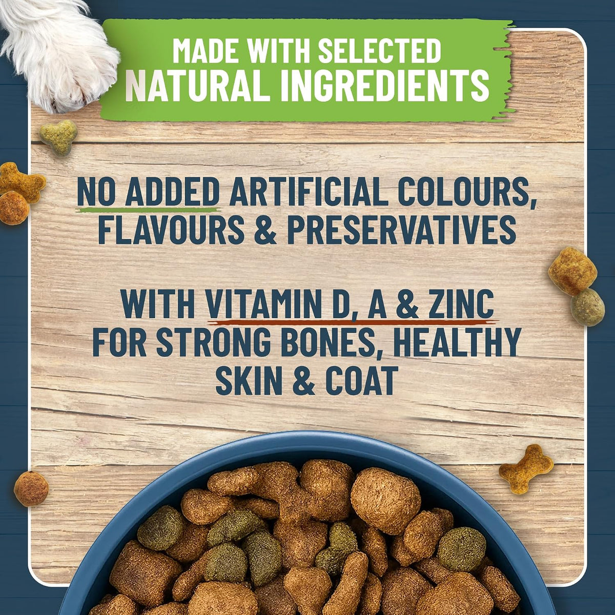 Dog food bowl with pet food, wooden board with text about natural ingredients and health benefits, and scattered dog treats.
