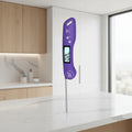A purple digital meat thermometer with a large backlit display is shown being held by a hand over roasted chicken and sliced steak, with promotional text highlighting auto-rotating backlit display and slide-in positioning.