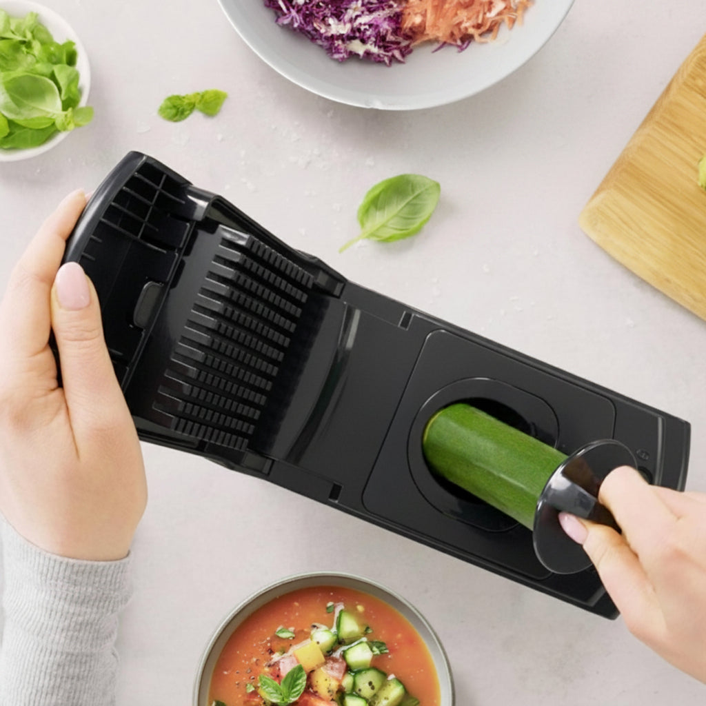 Person using a black vegetable chopper with a bowl of salad and ingredients on a white surface, featuring the 'fullstar' brand.