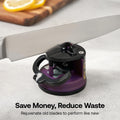 A kitchen knife being sharpened at a tabletop knife sharpener. The sharpener has a purple and black body with a circular base, shown on a light gray countertop with a blurred cutting board and lemon in the background.