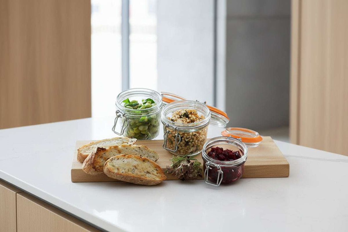 Jars of pickled vegetables on a wooden board with bread and utensils.