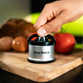 Hand using an 'Any Sharp' knife sharpener on a wooden cutting board with fruits in the background.