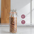 A clear glass clamp-lid jar filled with granola, shown on a kitchen counter with marketing callouts on the right describing features like an airtight lock seal, strong glass build, easy cleaning, and BPA-free safety.