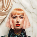A stylized portrait of a person with a short pink bob haircut and straight bangs, wearing a shiny black jacket over a patterned top. Large text on the right reads 'GREAT FOR STYLING ALL HAIR TYPES' over a bright lime green and teal graphic background.