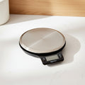 Digital kitchen scale on a wooden surface with a whisk and measuring spoons.