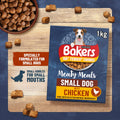 A 1kg package of Bakers Small Dog with Chicken dry dog food is displayed on a wooden board, surrounded by scattered kibble pieces and a bowl of dog food. The packaging is dark blue with red, yellow, and white branding, and includes a photo of a dog on the box.