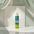 A can of Bed Head Tigi Master Piece Hairspray is shown on a white wood-textured background with sliced citrus fruits and leaves around it. Large text reads 'WITH AN EXOTIC, TROPICAL FRAGRANCE.