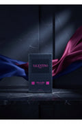 Valentino Uomo Born in Roma Extradose perfume box in dark blue packaging with pink lettering, shown in its plastic wrapping on a white background.