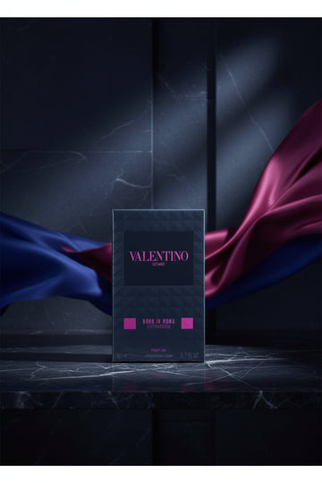 Valentino Uomo Born in Roma Extradose perfume box in dark blue packaging with pink lettering, shown in its plastic wrapping on a white background.