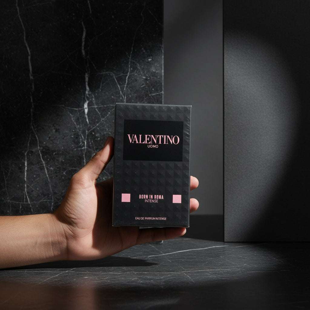 A hand holding a boxed fragrance product labeled VALENTINO UOMO and BORN IN ROMA INTENSE, photographed against a dark textured carpet background.